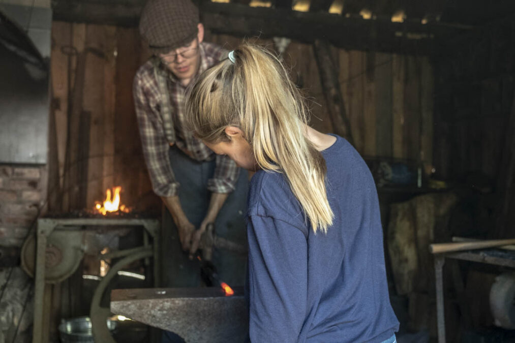 Girl learning metal forging in a blacksmith workshop at Folkenborg Museum during Barn og Dyr.